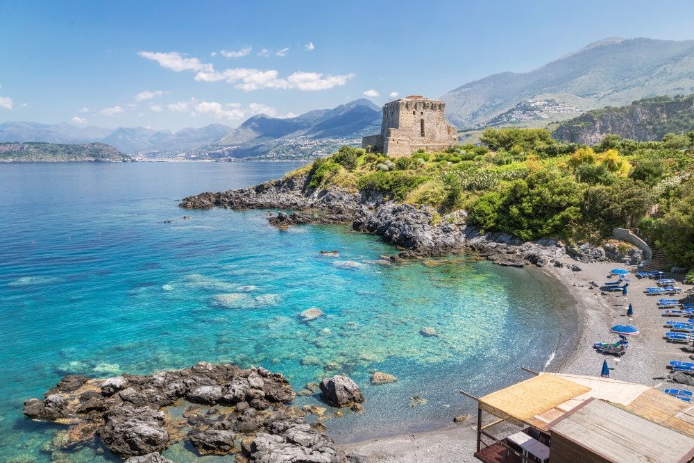 Una torre sulla costa, mare turchese e montagne della Riviera
